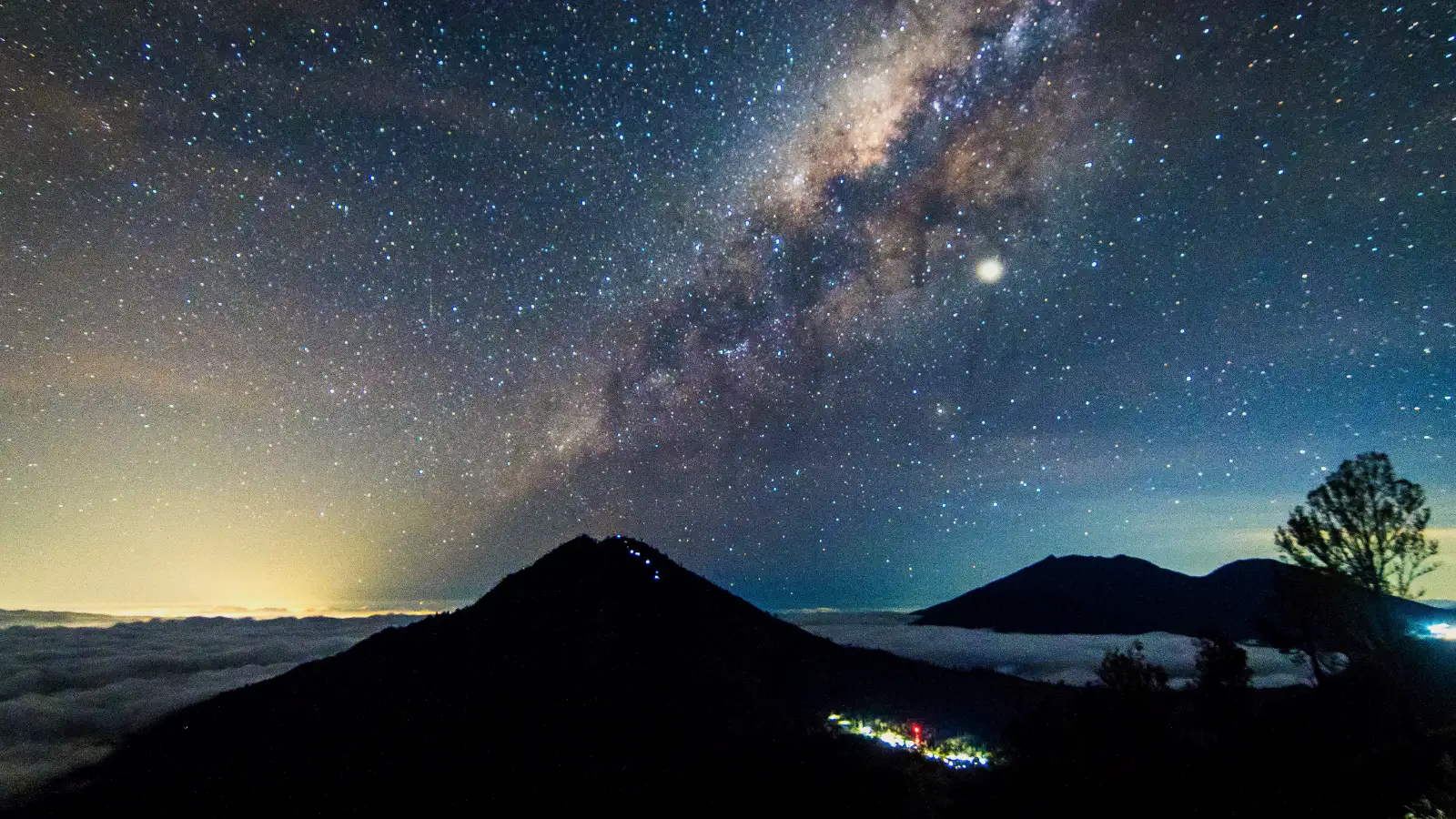 Night sky over Ijen volcano rim with glowing blue fire below