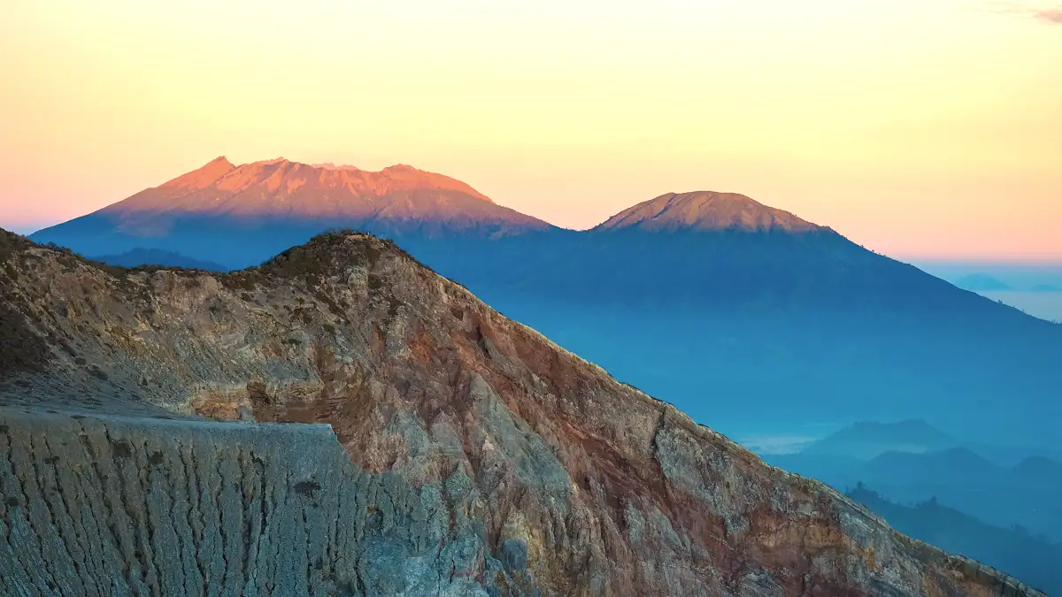 Jagged volcanic rocks and cliffs surrounding Ijen crater lake